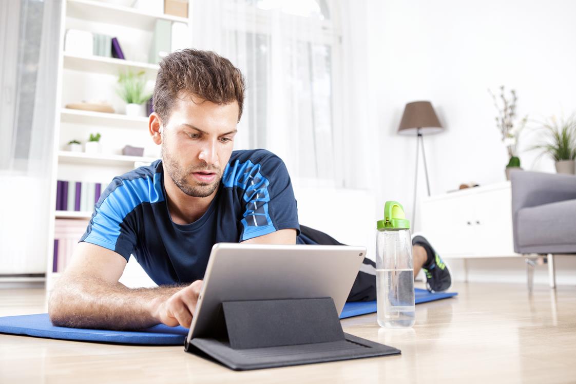 Handsome Young Guy Using his Tablet Computer While Lying on his Fitness Mat After Doing his Home Physical Exercise Routine.